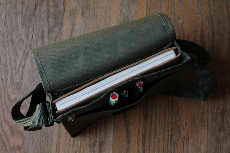 The messenger bag filled with a journal and several pens.