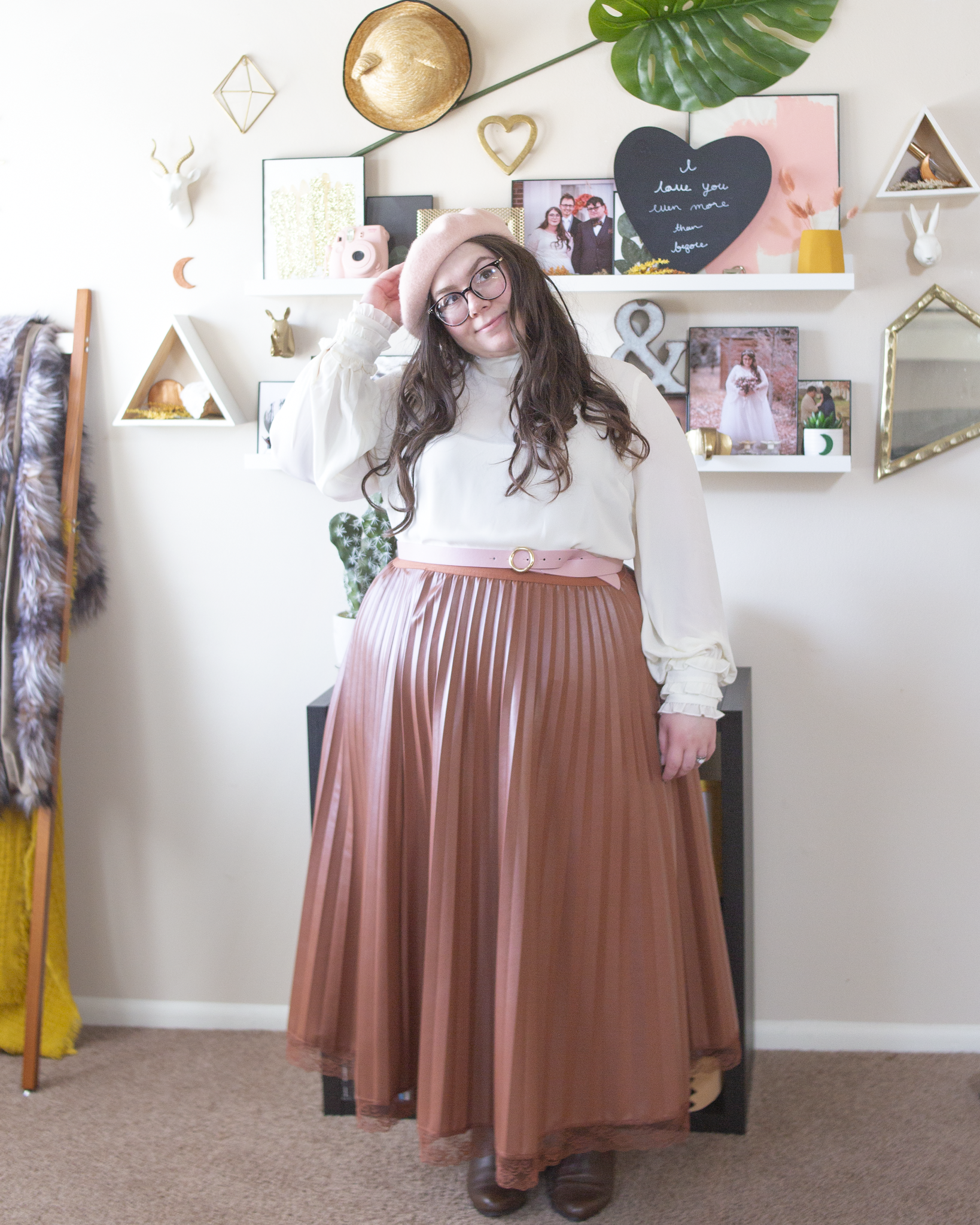 An outfit consisting of a pastel pink beret, a white high mockneck blouse with long puffy sleeves with ruffles at the sleeve hems, tucked into a cognac brown pleated midi skirt with a lace hemline, and brown chelsea boot.