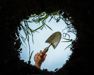 A hand holding a trowel over a hole. The view is from the ground up.