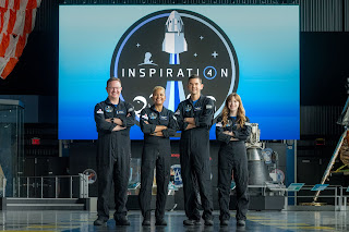 Four crew members standing in front of a large Inspiration 4 logo