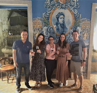 Três mulheres e dois homens com copos de vinho do Porto e painel de azulejo ao fundo com imagem da D. Ferreirinha