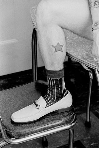 Black and white photo of a man's calf with simple star tattoo