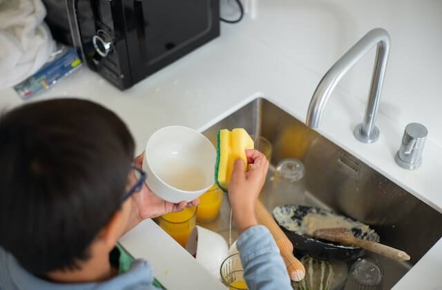 boy with glasses doing the dishes