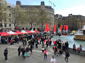 Red and white stall, and fountain with modest crowd in Trafalgar Square