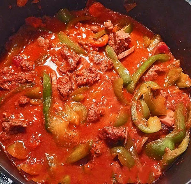 Italian sausage in cabernet sauce in a pot with peppers, onion and garlic with tomatoes