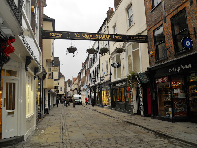 York, England. St. Nicholas Cathedral,  History, Architecture,  Streets, Wall, Walk, York is a small walled city situated at the middle of the busy railway route from Edinburgh to London. The city itself is very small and can be covered on foot twice in a day. That is what we did when we got there. Here are some pictures of the streets of York. Hartleys - the Best Sandwich Shop in York (As written on a board outside the shop). No doubt, it is the cutest though.Some dilapidated old ruins near the Museum Gardens. A lot of Ghost walks are organized here. The street leading towards the York Minster. See how empty they are. The entire population of York in 2007 was less than 2 Lakh people.Beautiful building enroute to the York Minster. On closer inspection, it turned out to be Grays Solicitors. Not too exciting.St. Wilfrid's Church opposite Gray's Solicitors. The construction of the Church was completed in 1864 costing around £10,000 - a little less than the tution fees for my MA.The York Minster Cathedral. It took us a while to locate the main entrance of this huge building. St. Michael le Belfrey Church besides the York Minster. A lot of these buidlings have been standing since the medieval times. The sign for the Ye Olde Starre Inn across stonegate -  the inn has been standing since the English Civil Wars in the mid-17th Century. The building itself (not in this picture) was once used as a hospital and mortuary. No wonder several ghosts haunt the premises. Trade Secret Salon near Coppergate. This was close to the Jorvik Viking Centre. West Cornwall Pasty Co. at the Coppergate Shopping Centre. Food abounds at every corner in York. Never make the mistake of eating too much on an outing. You will end up feeling wretched.York at night with brilliant moon high up in the sky. Well, it will not be fair to call it night though since it was barely 4:30 in the evening.The York city wall - ﻿more miles of this wall are intact as compared to the other cities in England.