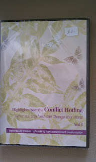 Photo of a DVD cover. It's a plastic case with a white cover with pale green leaves and butterflies stenciled on it. Near the bottom, in purple, it says, Highlights from the Conflict Hotline. What you say next can change your world. Volume 1. Featuring Miki Kashtan, co-found of Bay Area Nonviolent Communication.