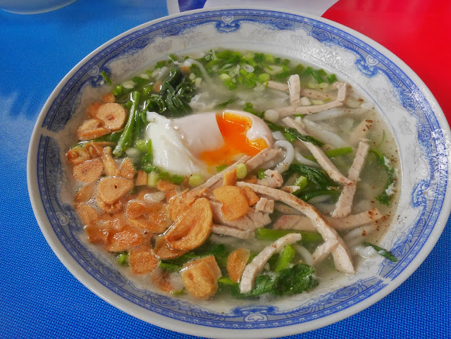 a bowl of laotian noodle soup with a fried egg, pork, and fried garlic