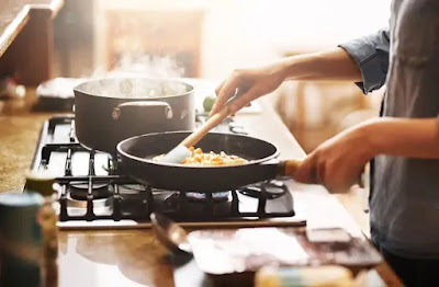 Woman cooking in non-stick cookware in a bright kitchen, emphasizing healthy and flavorful low-oil cooking techniques.
