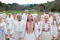 Still from the movie with white-clad men and women in a field