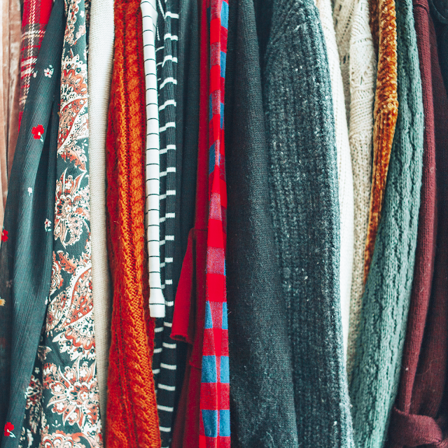 A flatlay of row of hanging sweaters and blouses.