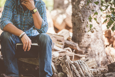 Hombre reflexionando al lado de un árbol y con un libro en la mano