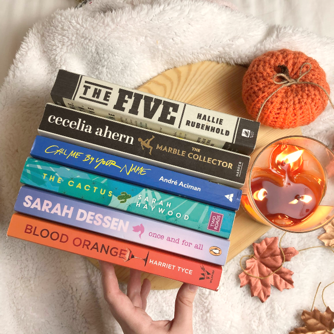 6 books in a stack with their spines facing up next to fake autumn leaves