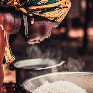 African woman with a headwrap cooking rice.