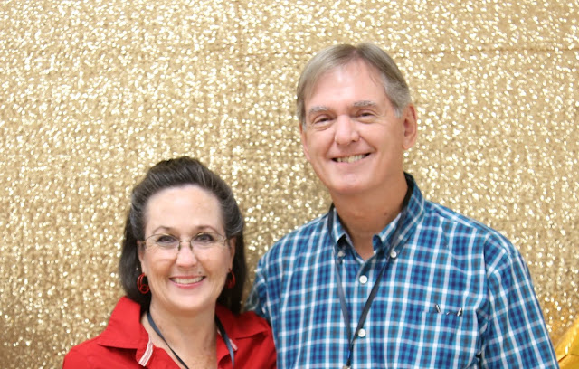 man in blue plaid shirt standing next to woman in red blouse