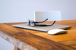 Glasses on a wood table with a laptop and a mouse