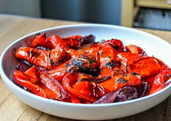 A bowl of red roasted peppers and onions.