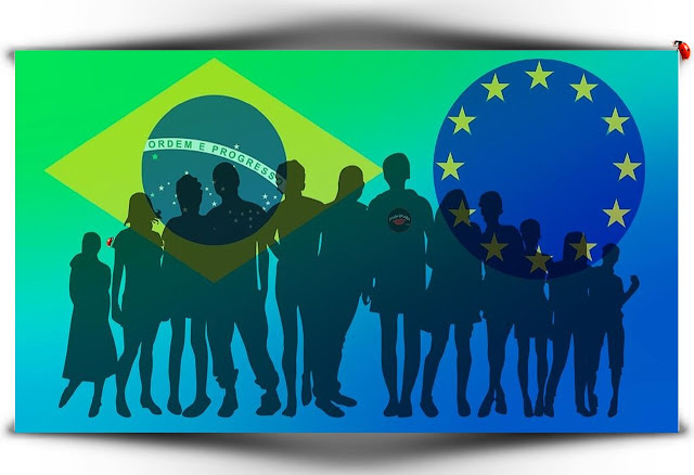 Pessoas tendo ao fundo a bandeira do Brasil e União Europeia