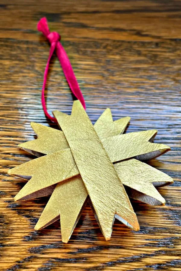 golden paper star ornament with fuchsia hanging ribbon displayed on wooden surface