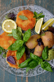 Knusprig frittierte Kohlrabi-Schnitzerl, neue Kartoffeln, Kräuterbutter, Zitronenspalten und Basilikum sind hübsch auf einem Teller aus Glas angerichtet.