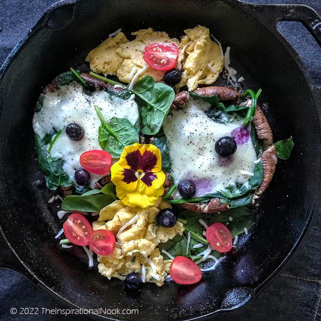 Portobello mushrooms steaks with scrambled eggs, spinach leaves, melted cheese, blueberries, cherry tomatoes and yellow pansies, cooked in a skillet
