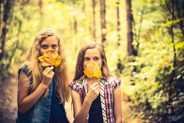 portrait two sisters holding yellow fall leaves in the woods