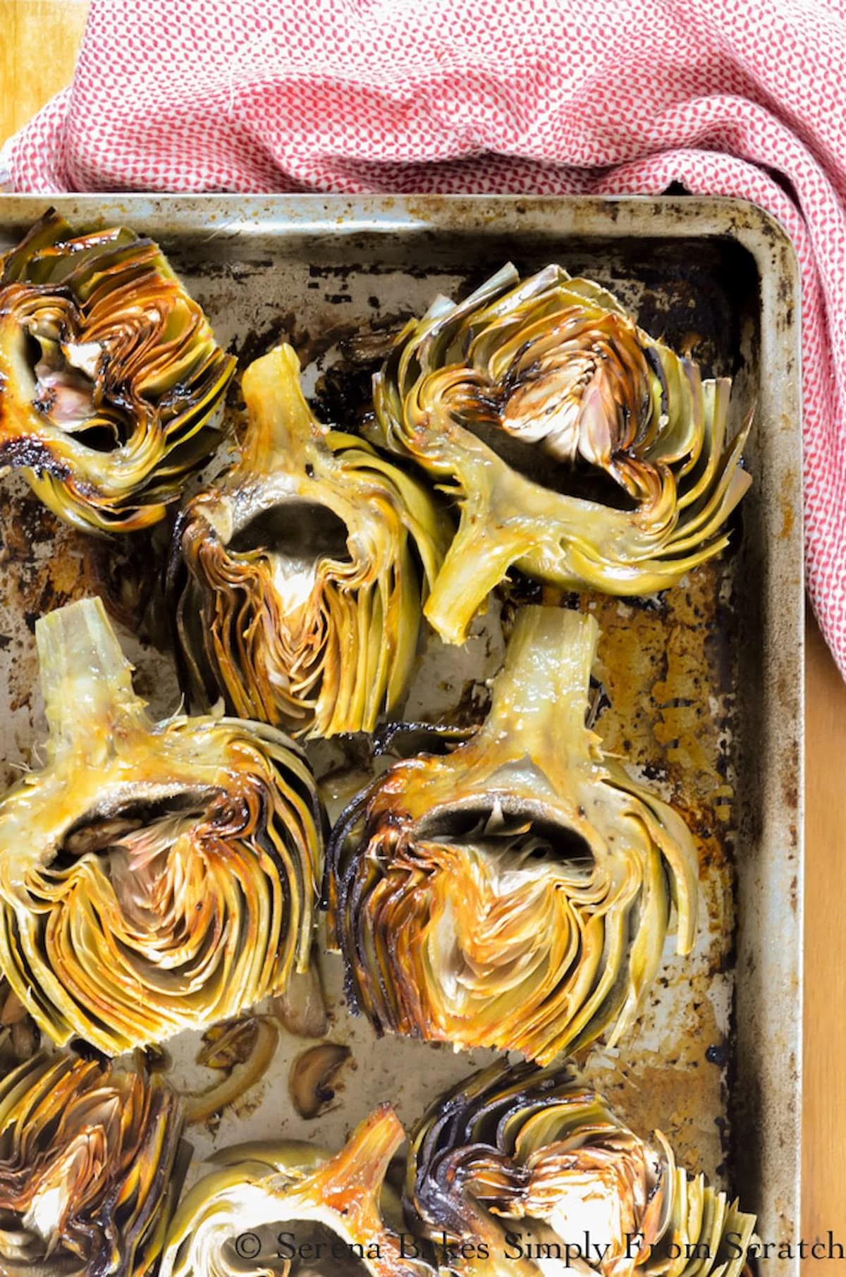 Roasted Artichokes with garlic on a baking tray with cut lemon.