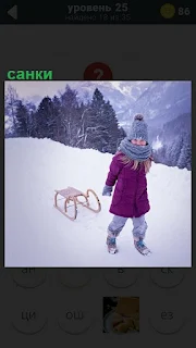 Девочка розовом пальто зимой с горы везет за собой санки