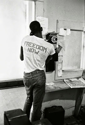 black and white photograph of African American man on pay telephone with "Freedom Now" on the back of his t-shirt, 1964