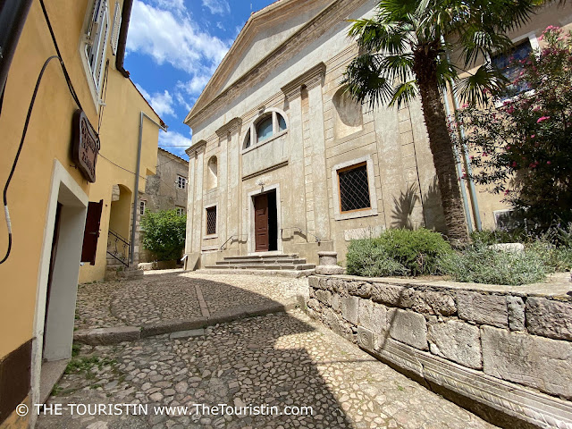 A church and houses on a narrow cobble-stoned lane.