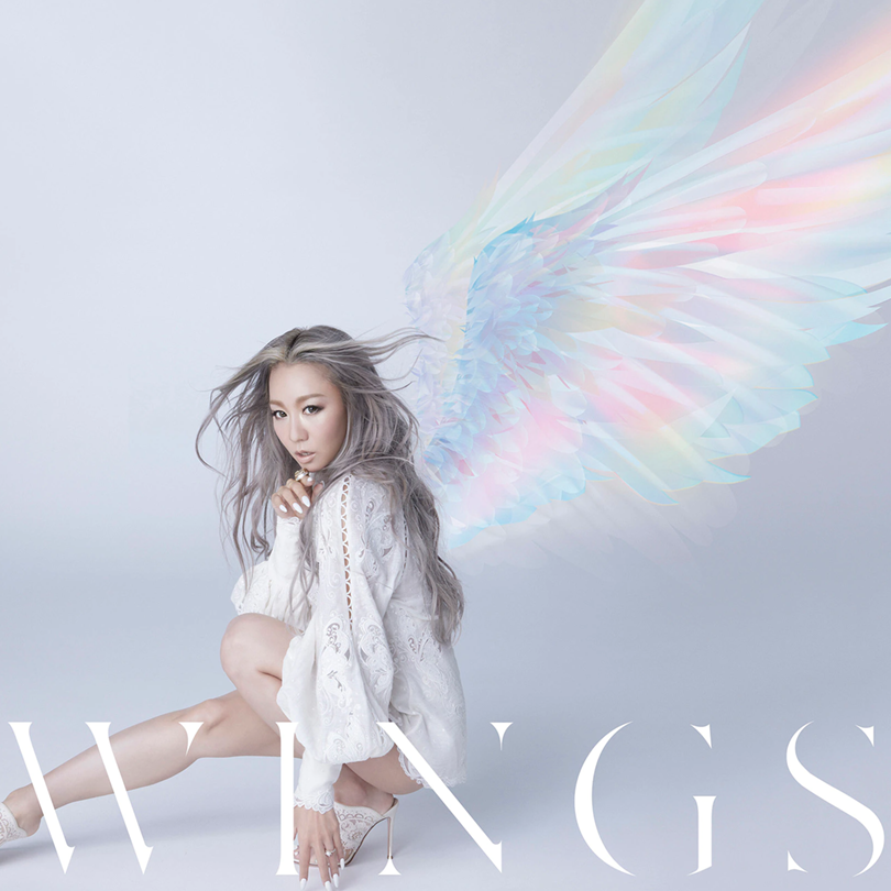 The CD+Blu-ray cover for Kumi Koda’s Wings, featuring Kumi crouched down on the floor, wearing a white dress with lace detailing, with multi coloured wings superimposed onto her back.