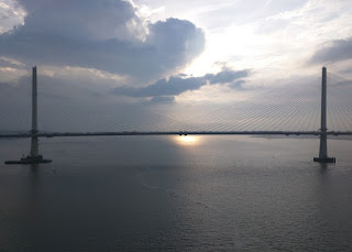 Sun reflecting on the waters of the Firth of Forth, framed by two pillars of the Queensferry Crossing, as seen from the Forth Road Bridge, Queensferry, Scotland