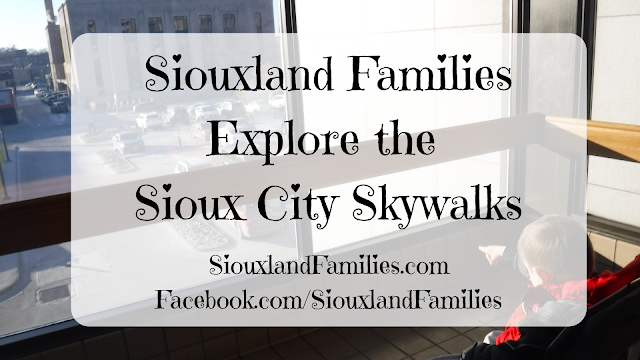 in bachround, a boy in a stroller points out the window from the Sioux City Skwalk System in downtown Sioux City Iowa, in foregound the words "Siouxland Families Explore the Sioux City Skywalks"