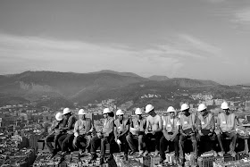 Black and white photo of workers on the skyscraper with the city skyline in the background