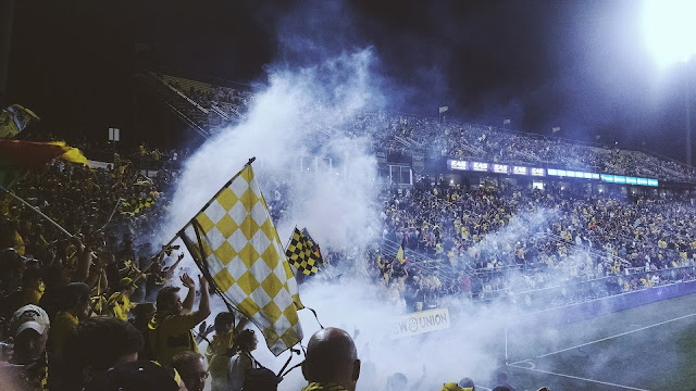 Football stadium where people are waving flags in smoky atmosphere