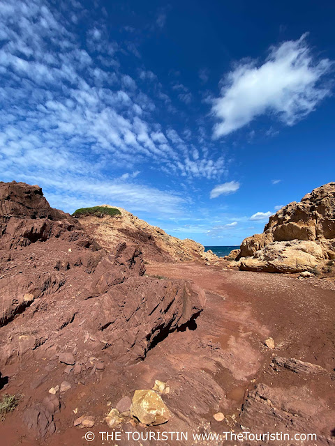 Red and golden sandstone cliffs under a blue sky with a few white fluffy clouds.