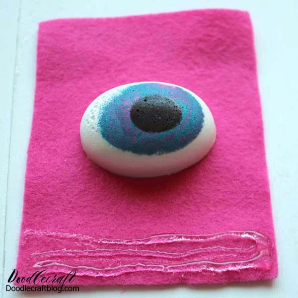Cut a piece of felt larger than the eyeball and hot glue the eye in the center.  Then add some hot glue to the bottom edge of the felt.