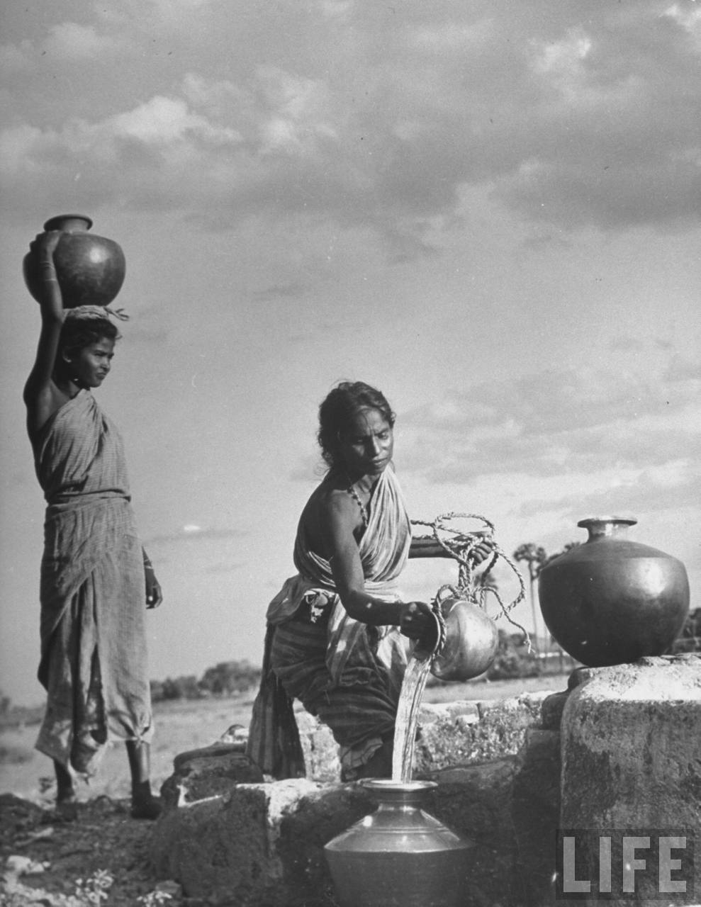 Indian Village Women Pouring Water From Village Well Into Their Jugs To Be Carried On Their Head 