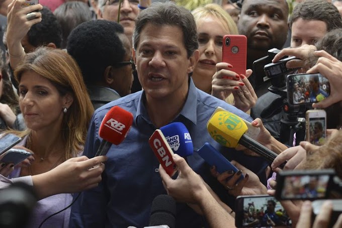 Com camisa azul, Haddad vota e faz sinal de vitória