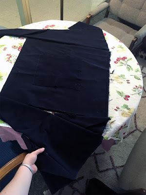 Several panels of blue-black velvety fabric laid out on a table; one side has a long triangular gore and a smaller, wider gore on the outside; the other has two smaller, slimmer triangular gores on either side of the long gore, making it flare out more dramatically from the center rectangle.