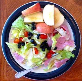 Plate of salad including lettuce tomatoes blueberries apples ham