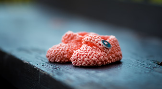 pair of baby's pink knit shoes on bench