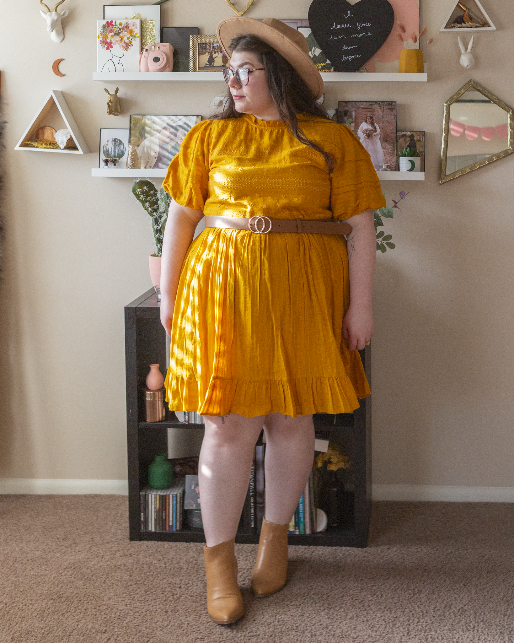 An outfit consisting of a camel brown wide brim fedora, a mustard yellow puff sleeve dress with lace embroidery mini dress and camel brown pointed toe Chelsea Boots.