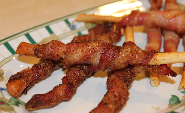 Bacon-wrapped breadsticks on a plate that has green stripes around the edge.