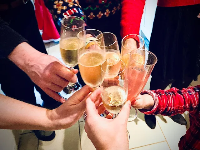 5 hands holding a glass of champagne together for cheers and one little hand joining in with a plastic cup with pink lemonade