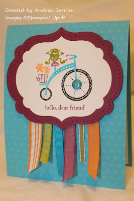 Turquoise card with orange, purple, green and turquoise ribbon. Colorful focal image of a frog riding a tricycle with the sentiment "hello, dear friend."