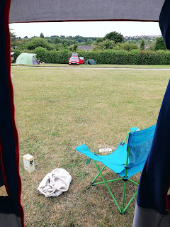 view from a tent doorway, a couple of vans, a hedge. blue sky