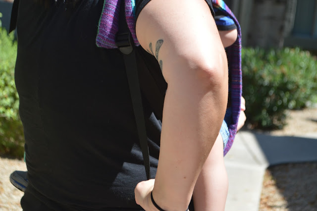 Image is a close up where woman is seen pulling down on the webbing in the shoulder harness of an onbu carrier worn in front