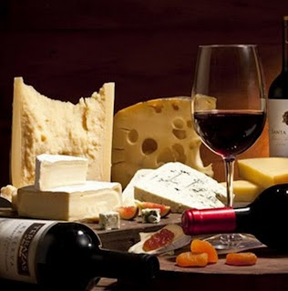 Foto com uma mesa repleta de produtos regionais de portugal: vinhos, azeite, charcutarias, fumeiros, enchidos, queijos, pães, frutos secos e uma taça de vinho maduro tinto.