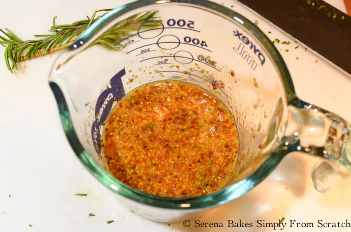 A glass measuring cup with Grainy Dijon Mustard, Honey, Apple Cider Vinegar, Rosemary, Salt and Black Pepper mixed together.